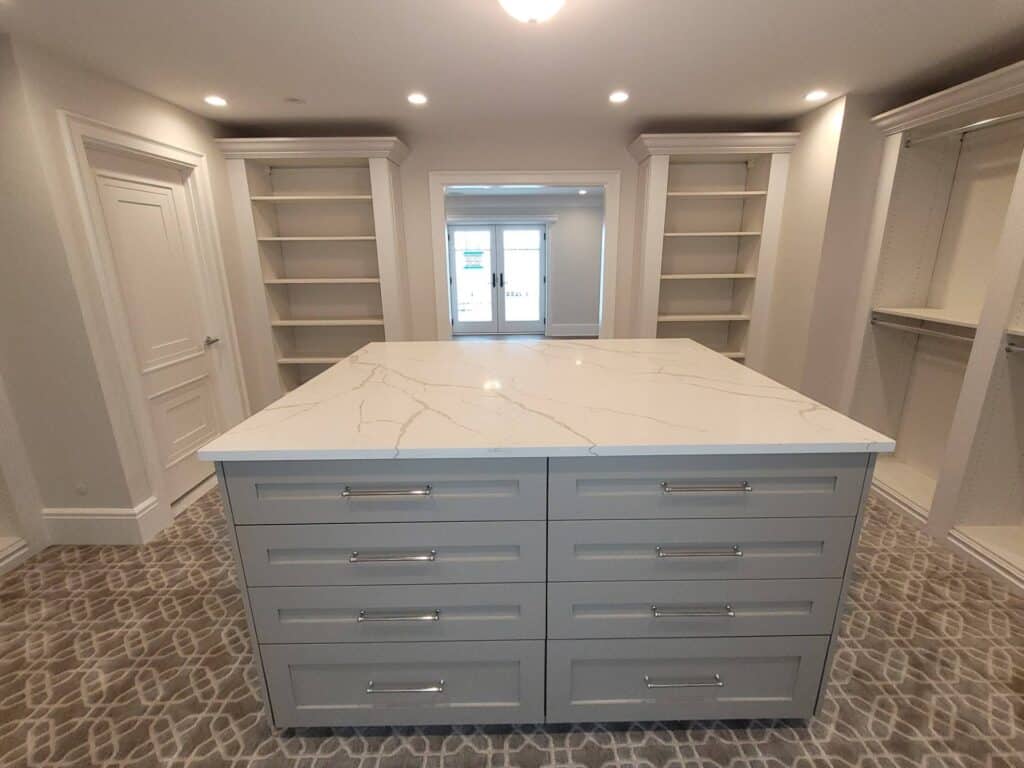 Custom walk-in closet with built-in shelves and marble-topped island for organized storage.