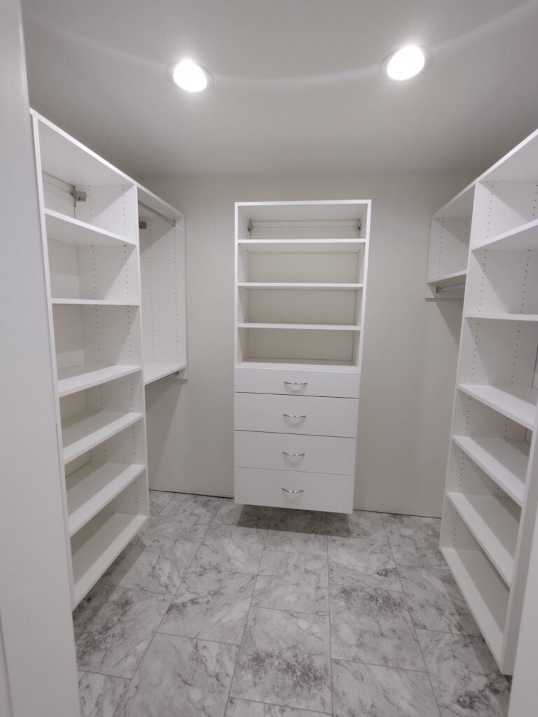 Spacious walk-in closet with white shelving and drawers for organized storage.