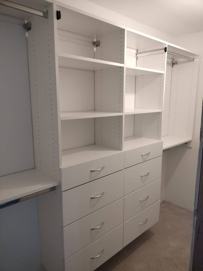 Custom white closet storage with drawers and adjustable shelves for organized wardrobe space.